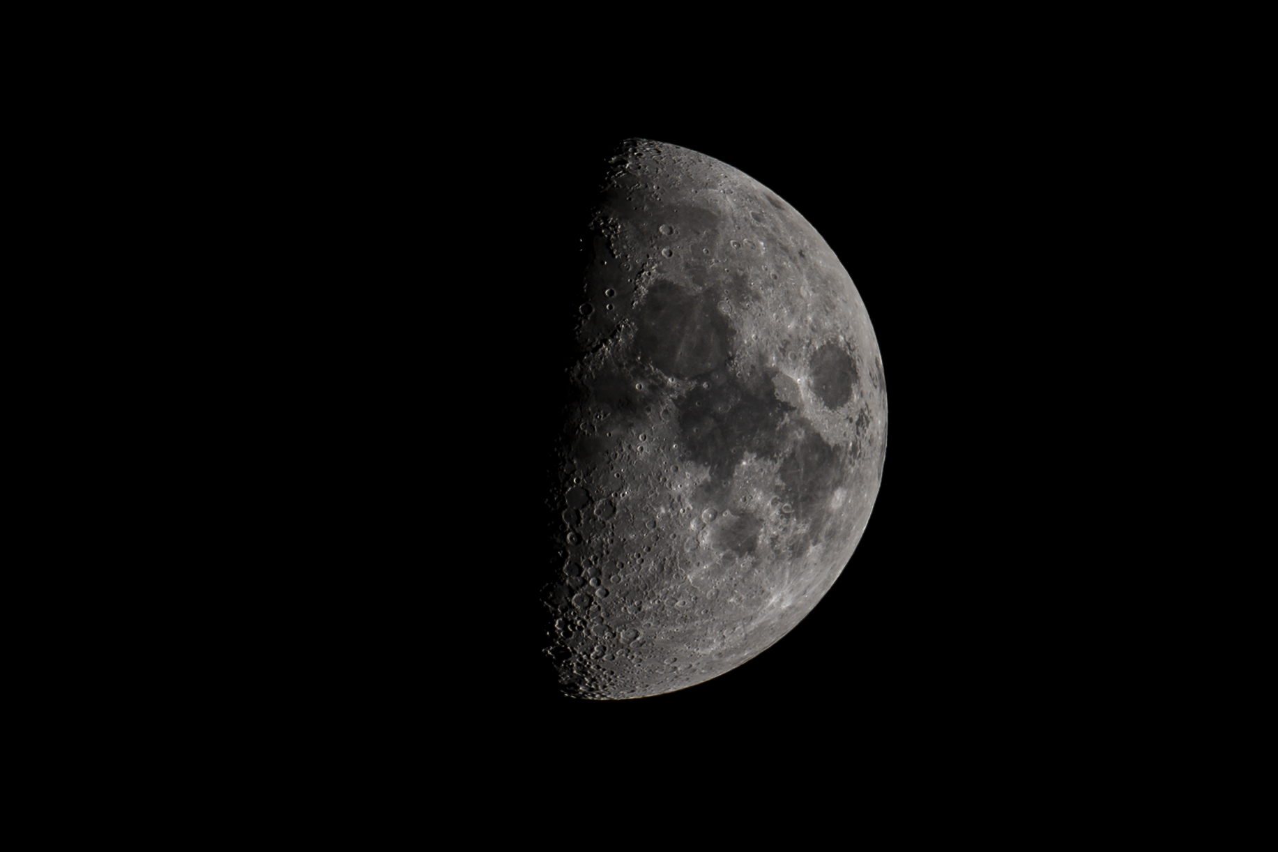 A detailed half-lit moon against a black sky, photographed by Logan Petrock.